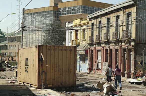 Residents walk past a shipping container washed up by a wave caused by an earthquake in Talcahuano Port.