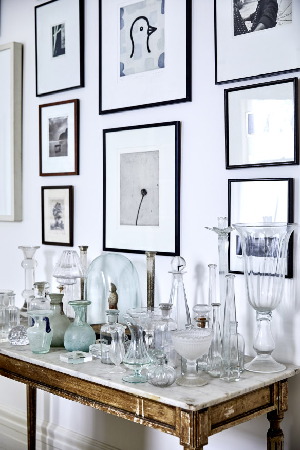 An antique, marble-topped French table displays a collection of Collison’s glassware. Above it are works by artists including Lee Miller and Max Dupain.