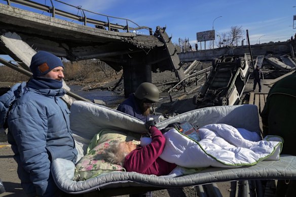 Volunteers pass an improvised path under a destroyed bridge as they evacuate an elderly resident in Irpin, northwest of Kyiv.  