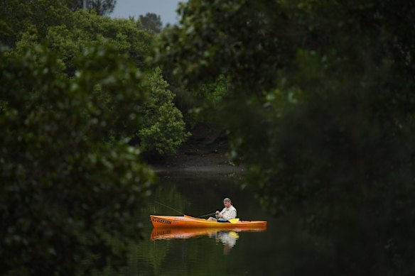 A man fishing from his small boat on the Cooks River at Kendrick Park in Tempe, Sydney.