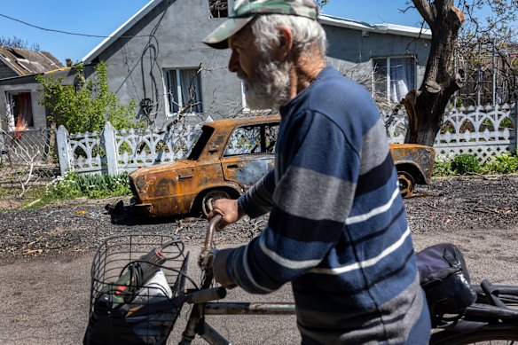 Sergii, 63, walks his bike past a neighbor's destroyed car in Novovorontsovka.
