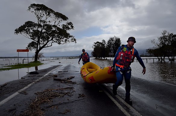 SES rescuers carry their boat from the floodwaters that have partially submerged Bolong Road at Shoalhaven Heads, NSW.