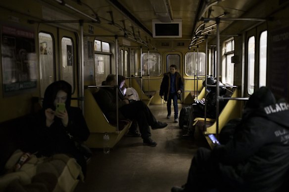 People use their phone as a boy plays in a subway car parked inside a station being used by residents as a bomb shelter in Kyiv.