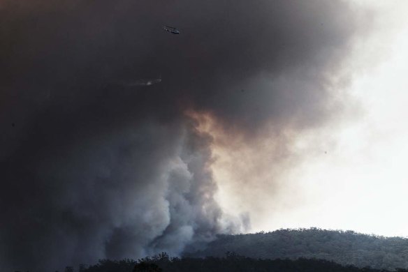 A helicopter is barely visible through the smoke of an out-of-control bush fire, Sth West of Wandandian