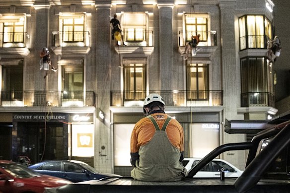 A commercial abseiler checking his phone while others are tethered from a building cleaning windows. Despite lockout laws ending last night, the CBD was mostly empty aside from service workers.