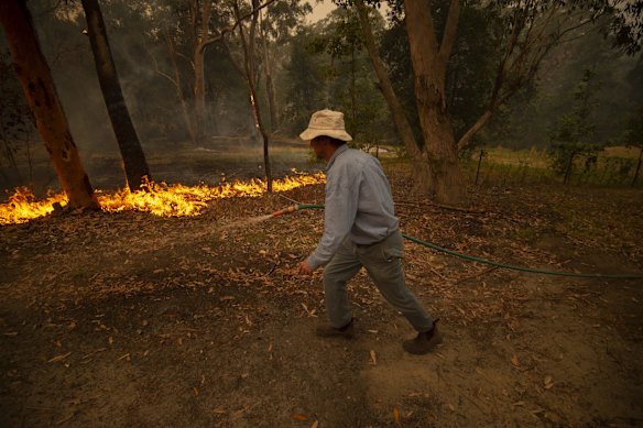 Rob Meggs mops up on his property after the Wrights Creek fire had swept through Kyola Rd on the outskirts of Kulnura, west of the Central Coast.