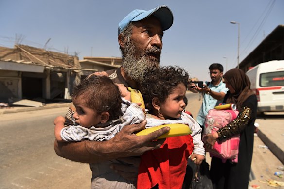 A man carries two children after climbing off a truck at a screening point after being rescued by Iraqi forces in West Mosul.