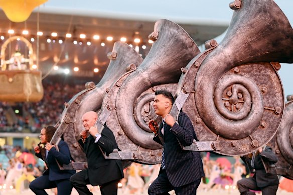 Performers carry large musical instruments.