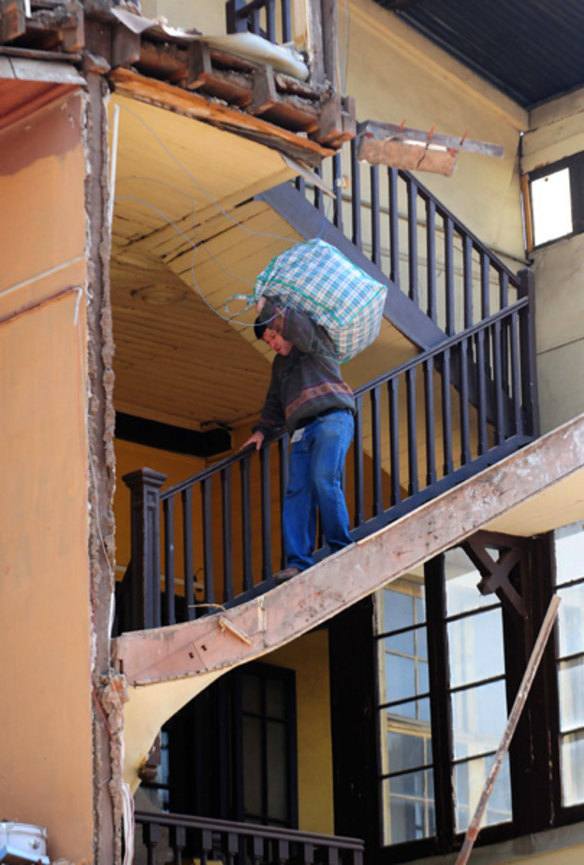 A man carries personal belongings as he goes down the stairs of a damaged house in Santiago.