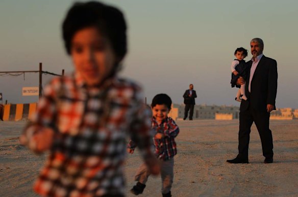 Khalid Mishal (right) holds his one year old granddaughter Sara whilst going for a walk with his grandsons Bara 4yrs (left) and Saad 2yrs (2nd from left) in the suburban streets of Doha, Qatar. A bodyguard provides security in the distance.