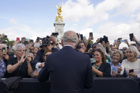 King Charles III, back to camera, greets well-wishers as he walks by the gates of Buckingham Palace. 