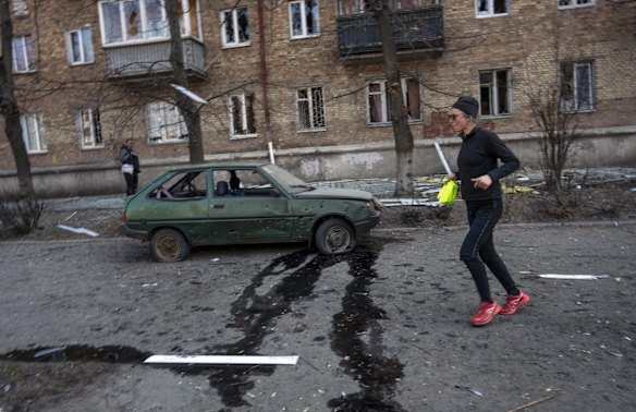 A woman exercises near a car and apartments damaged by shelling in Kyiv.