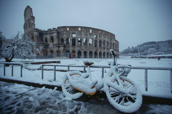 A bicycle is parked in front the ancient Colosseum during the snowfall in Rome.