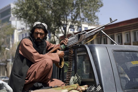 A Taliban fighter sits on the back of vehicle with a machine gun in front of the main gate leading to the Afghan presidential palace, in Kabul, Afghanistan. The U.S. military has taken over Afghanistan's airspace as it struggles to manage a chaotic evacuation after the Taliban rolled into the capital. 
