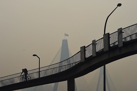 A smoke haze fills the sky as cyclists and pedestrians make their way along the overpass over the Anzac Bridge in Rozelle, Sydney.