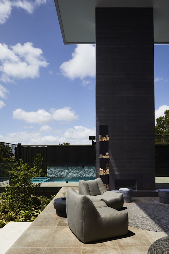 The rear of the home opens to an entertaining area with another towering fireplace and views to the pool and tennis court. The chairs are from Parterre.