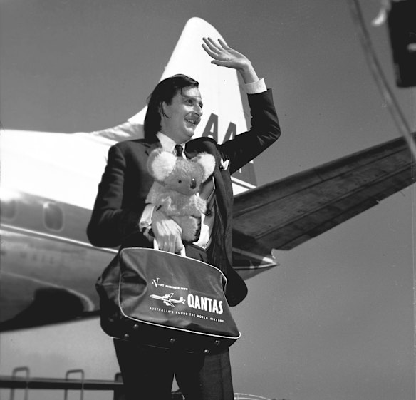 Australian entertainer Barry Humphries holding koala bear and Qantas bag waving on arrival in Melbourne in 1965. 
