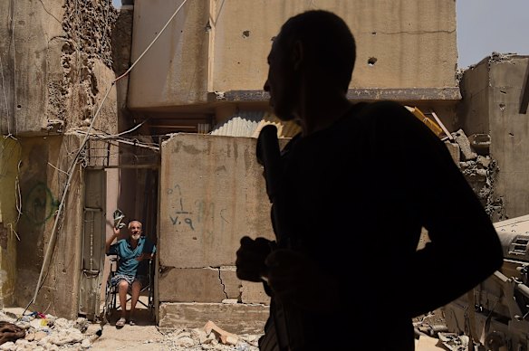 Unable to walk, Abdulsalam Abufader 73 (right) talks with Iraqi Special Forces as he sits in his wheelchair at the entrance of his home in West Mosul.