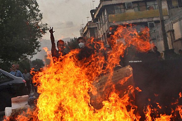 In this photograph posted on the internet, an Iranian protestor flashes the victory sign from behind a public trash bin set on fire at an anti-government protest in Tehran, Iran Saturday June 20, 2009.