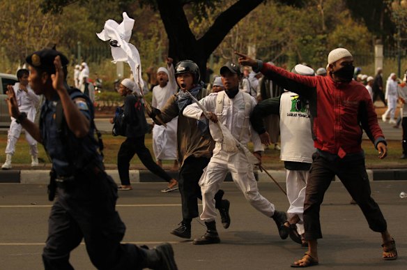 An Indonesian security guard from the US Emabassy attempts to flee as he is threatened by a group of protestors throw rocks as Indonesian police release tear gas at anti American protests infront of the US Embassy in Jakarta, Indonesia.