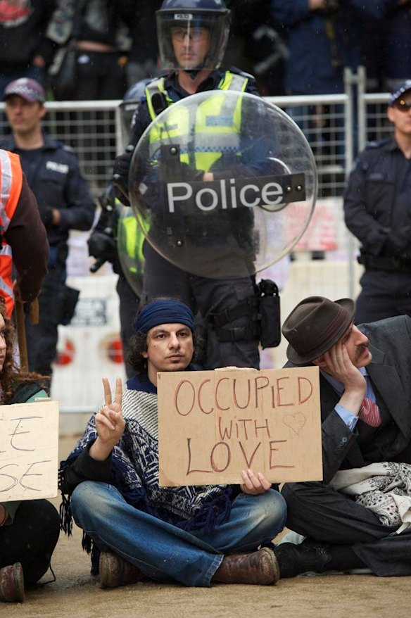 Police stand behind protesters bearing signs.