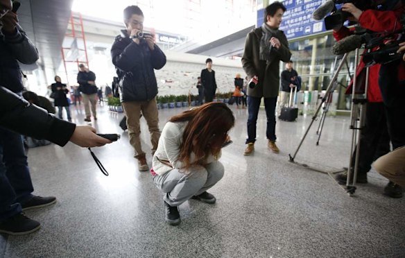 Journalists attempt to interview a woman who is the relative of a passenger on Malaysia Airlines flight MH370, as she crouches on the floor crying, at the Beijing Capital International Airport in Beijing.