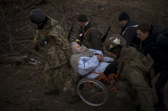 Ukrainian soldiers and militia members carry a woman in a wheelchair as the artillery echoes nearby, while people flee Irpin on the outskirts of Kyiv, Ukraine.