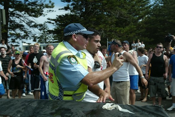 The man is shielded by an officer wielding capsicum spray.