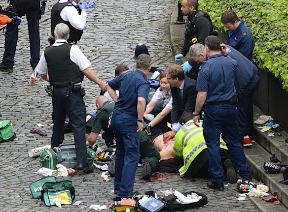 Conservative Member of Parliament Tobias Ellwood, centre, helps emergency services attend to an injured person outside the Houses of Parliament.