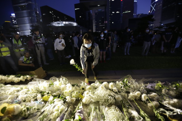 A woman places a flower at a vigil for student Chow Tsz-Lok in Hong Kong on Saturday 