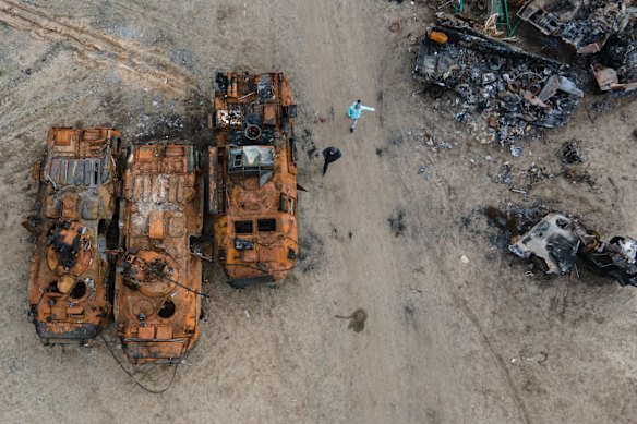 A man and a girl walk past burnt military APCs in a field where destroyed vehicles are being brought in Bucha, Ukraine.