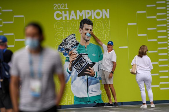 A spectator places a mask over the face of 2021 AO champion Novak Djokovic. Djokovic was controversially deported from Australia and unable to defend his title.