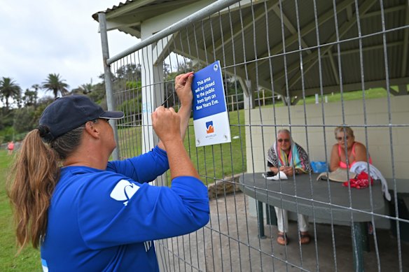 A Waverley Council worker puts up warning signs on huts that are fenced off as a precaution against COVID-19 on New Years Eve at Bronte Beach in Sydney.