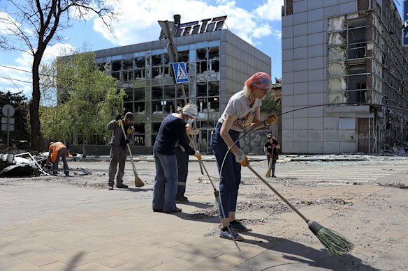 Volunteers clean a street next to damaged buildings in Mariupol.