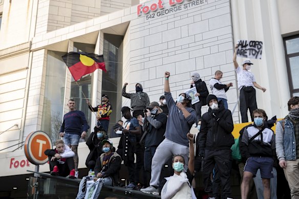 Protestors climb on to the roof of a building in George St, as thousands rally in support of the Black Lives Matter movement.