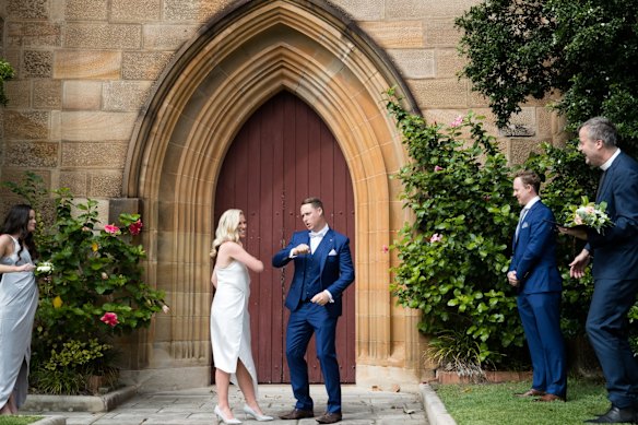 Newlyweds Brigette Leech and Matthew Selby jokingly go for an elbow touch instead of a kiss. They are watched by Minister Justin Moffatt, and their siblings, Charlotte Leech and Hugh Selby, at the Garrison Church in Sydney. 