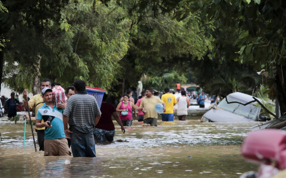 Residents in Honduras wade through floodwaters, past inundated vehicles.