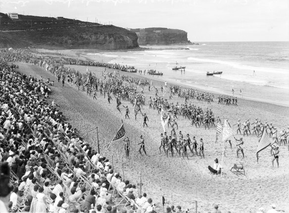 Crowds watch the Australian surf lifesaving champions at Newport Beach in Sydney, on March 14, 1953. Edwin “Buddy” Adolphson can be seen with his Stars and Stripes flag front and centre of the assembled clubs.