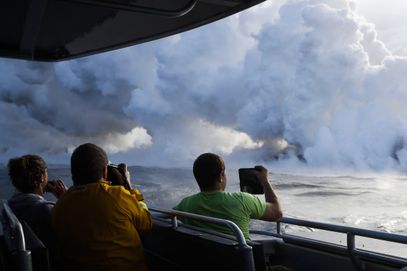 People take pictures as lava enters the ocean, generating plumes of steam near Pahoa, Hawaii.
