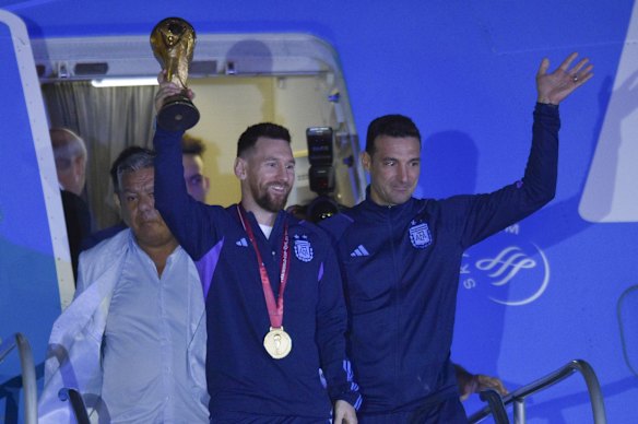 Argentina's Lionel Messi holds the FIFA World Cup trophy as he deplanes, with coach Lionel Scaloni, in Buenos Aires, Argentina.
