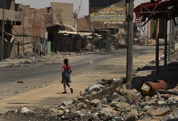 A girl walks across a street surrounded by debris and destroyed buildings in West Mosul.