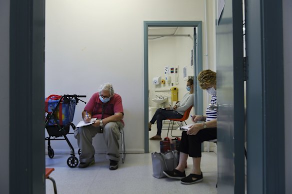 Frances Callen (R) fills out a form as she waits for a coronavirus test at the Covid-19/Flu Assessment Clinic.