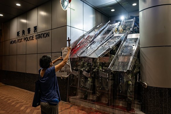A woman holds a cross in front of the Mongkok Police Station as riot police holding shields stand guard during a standoff with protesters after an anti-government rally in on September 1, 2019 in Hong Kong, China. 