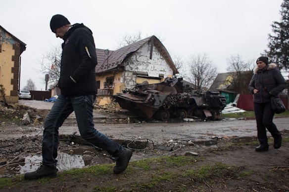 Local residents walk by a burned Russian armoured personnel carrier in Ploske.