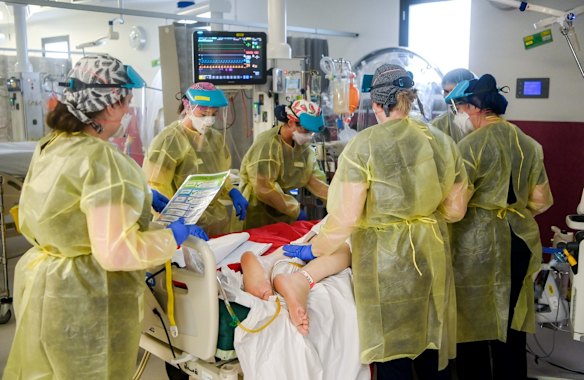 Nurses prepare to roll a patient in their bed as part of their COVID-19 treatment process.