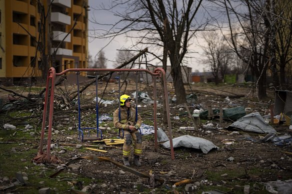 A firefighter sits on a swing next to a building destroyed by a Russian bomb in Chernihiv.