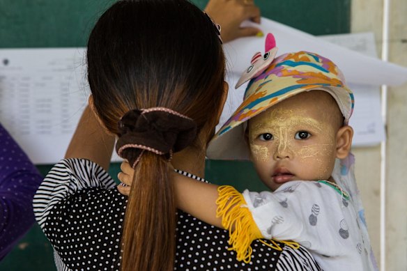 A woman holds a baby as she looks through names on a voter's registration list at a polling station in the village of Dala, Myanmar.