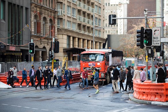 Pedestrians navigate the construction of the light rail at the intersection of George Street and Bridge Street, as heavy trucks lug construction material in and out of the area.