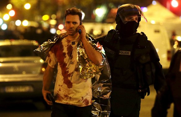 A French policeman assists a blood-covered victim near the La Bataclan concert hall.