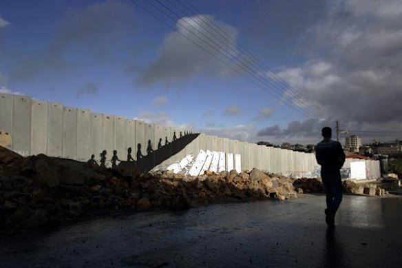 A Palestinian man walks next to a section of Israel's separation barrier featuring Banksy's graffiti.